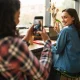 Seorang pelanggan wanita memotret temannya di kafe menggunakan smartphone, ilustrasi nyata dari penerapan strategi User-Generated Content (UGC).