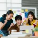 Tim Digital Agency yang kompak merayakan keberhasilan kampanye di depan laptop, menunjukkan efisiensi dan sinergi tim agensi dibanding in-house.